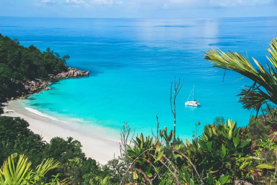 Elevated view of a vibrant turquoise bay, white sandy beach, and green tropical hills along the Seychelles coastline.