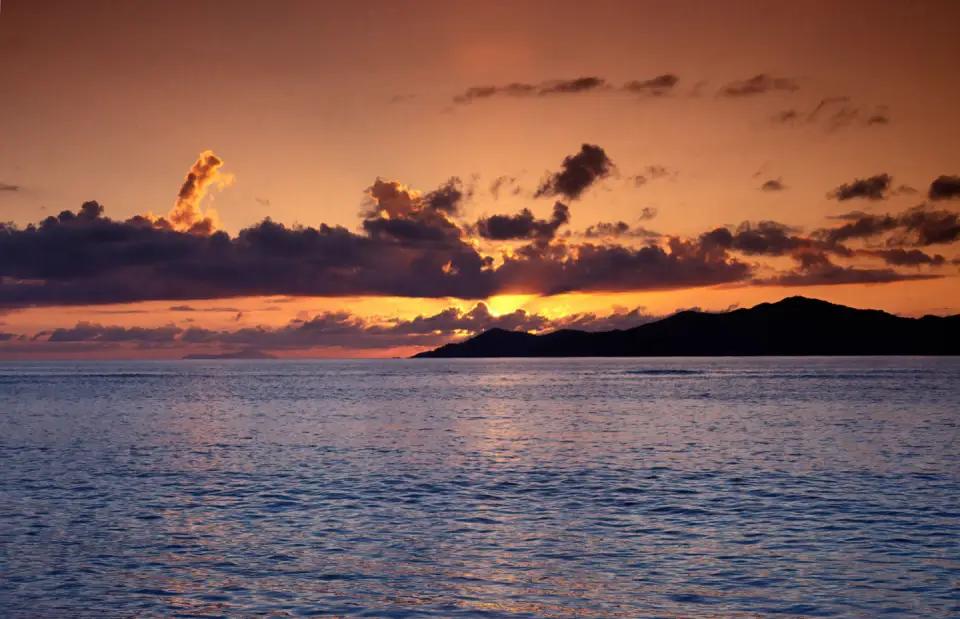 Golden sunset over the Indian Ocean, with distant tropical islands silhouetted against an orange and purple sky.